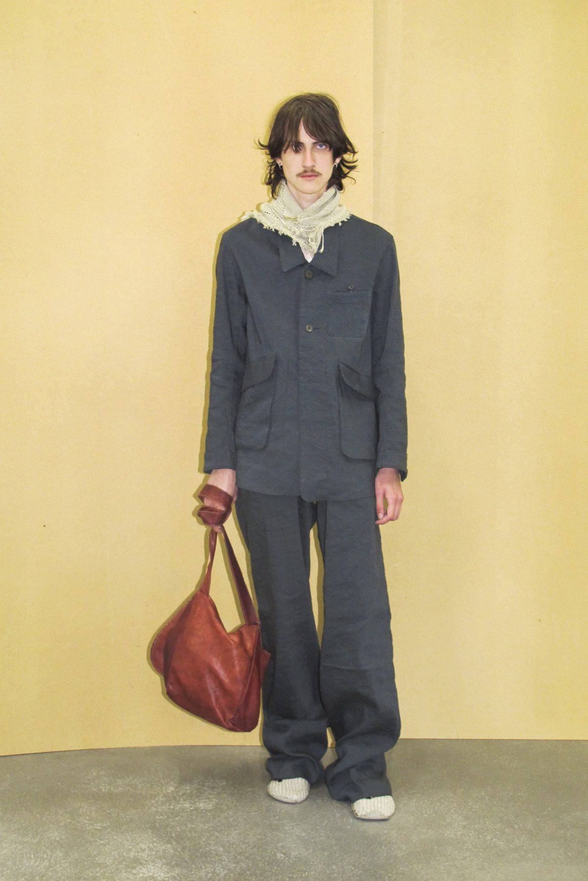 Model wearing a grey jacket, grey loose trousers and brown leather bag