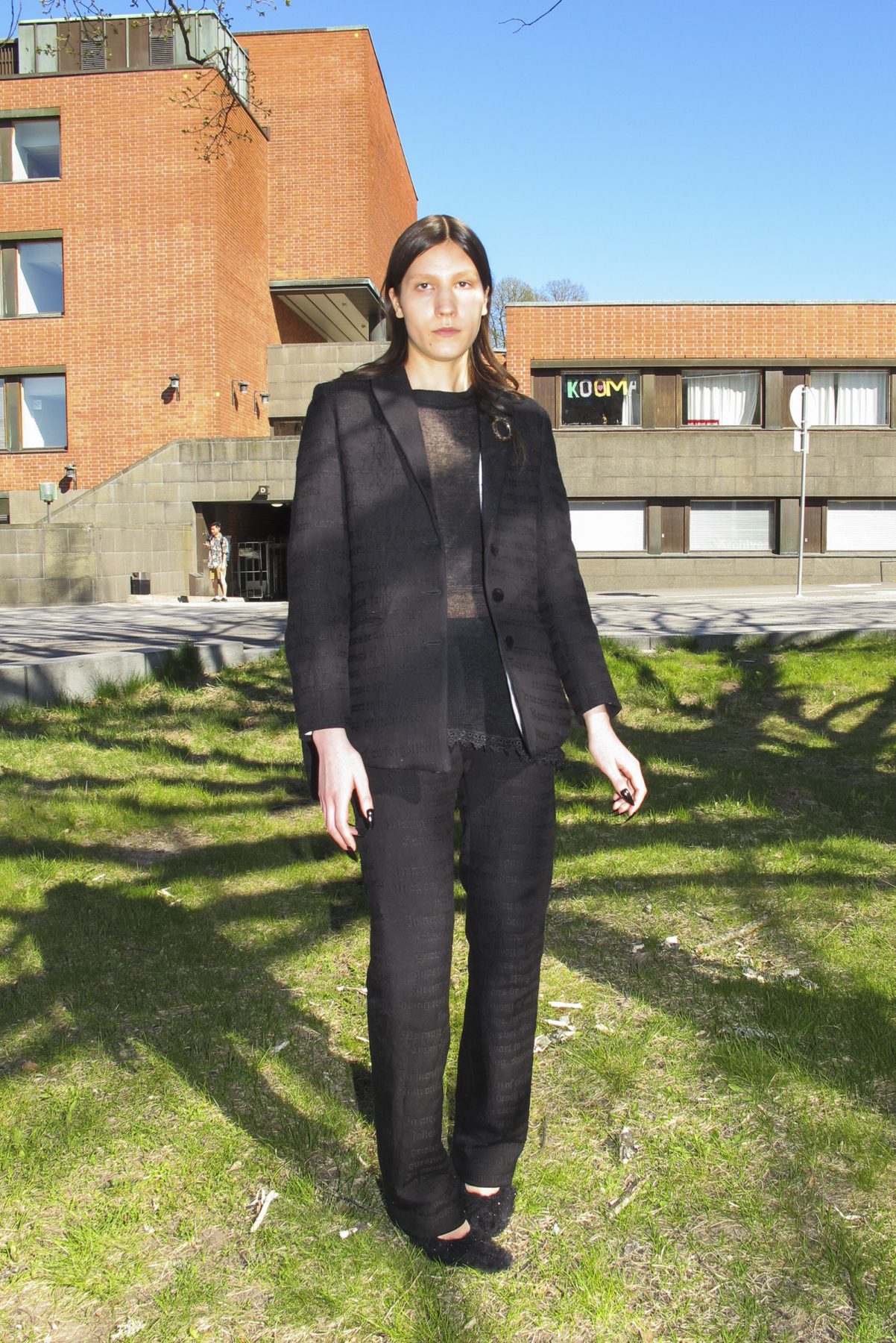 Model is wearing a black cropped suit jacket, sheer shirt underneath and black suit pants