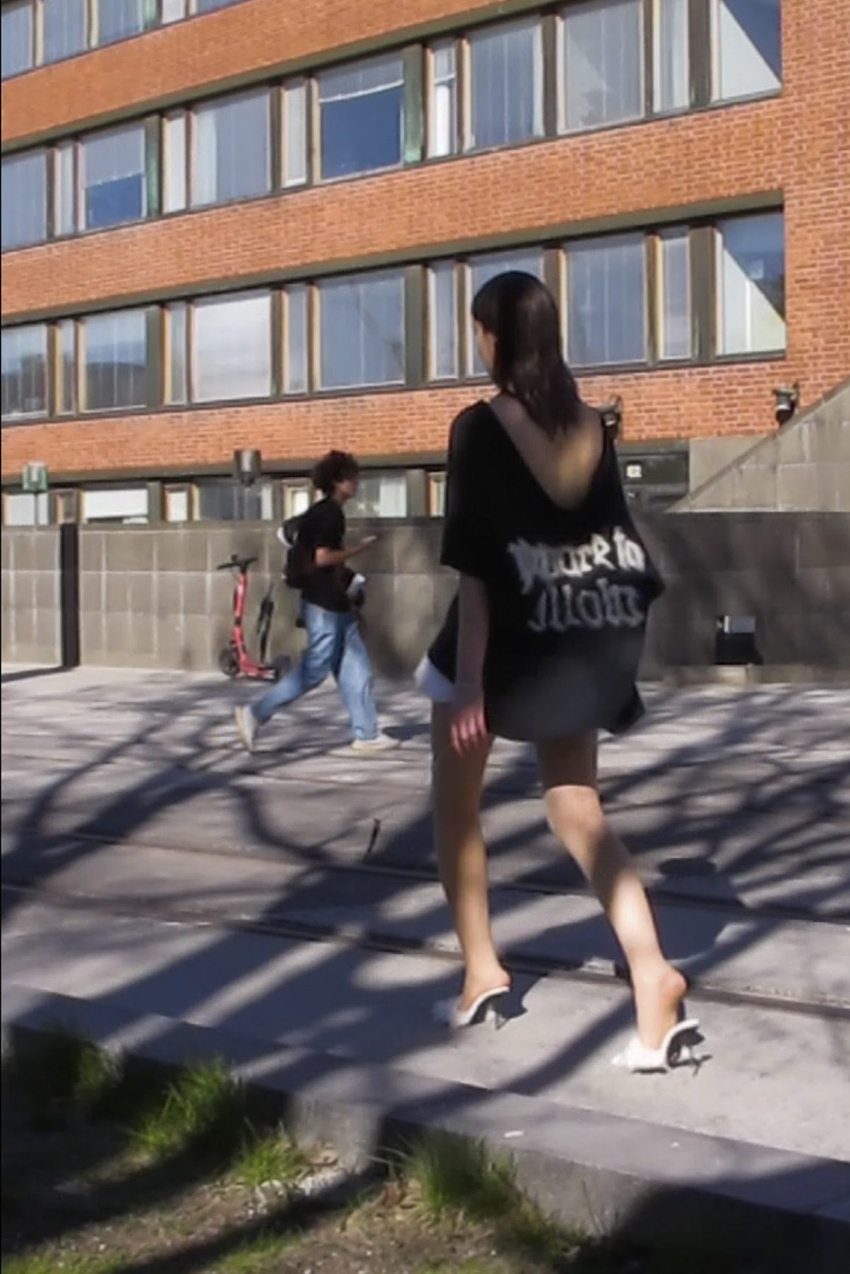 Model is walking and wearing a black t-shirt with text and short white skirt