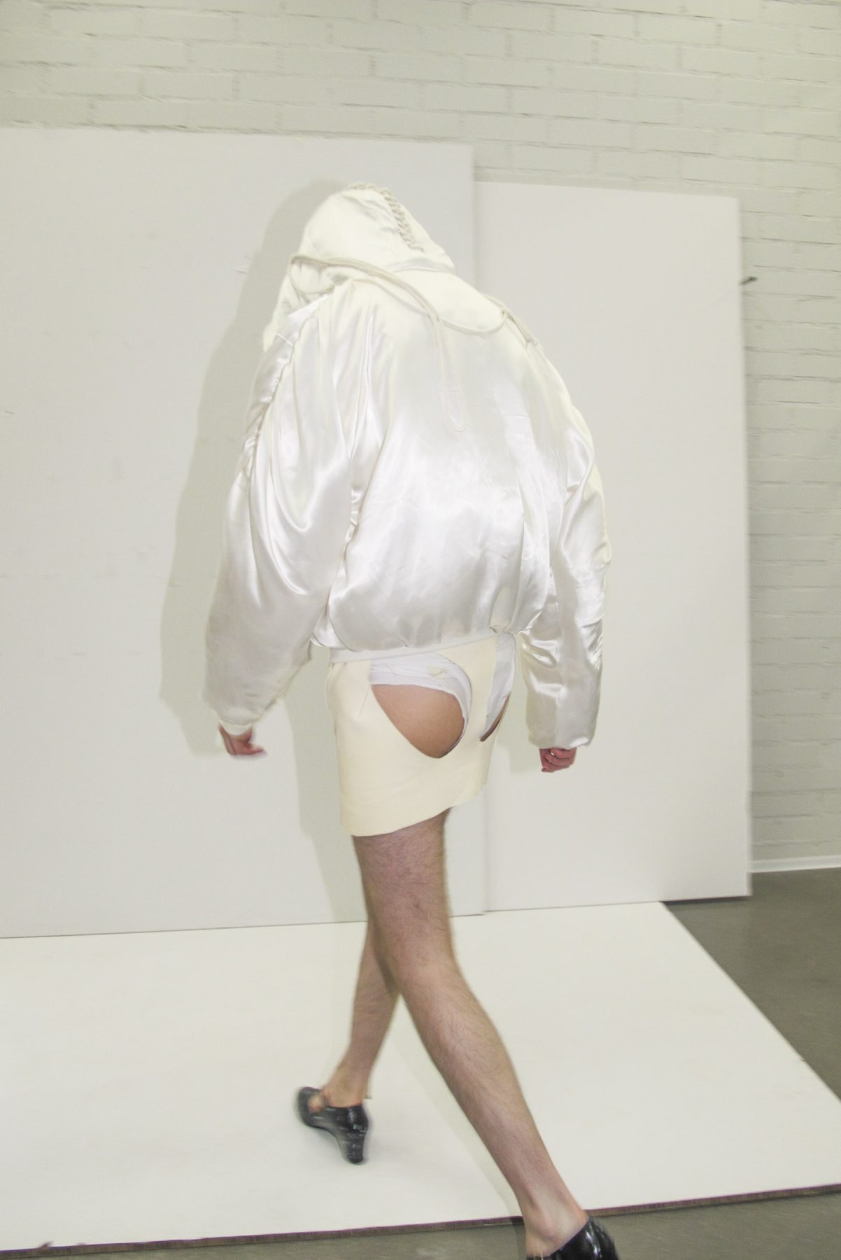 Back of model wearing butt-exposing short leather skirt and puffy white jacket