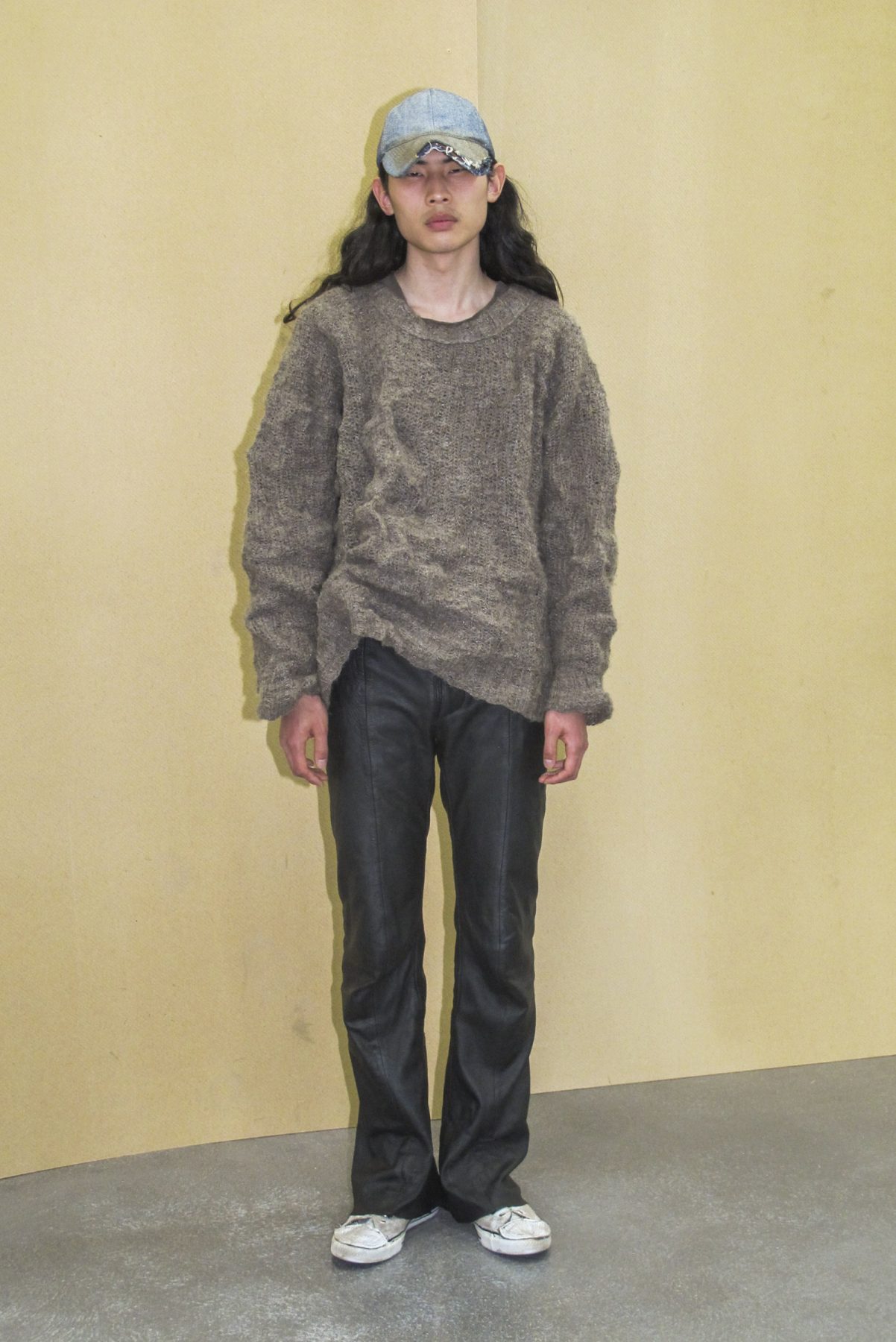 Photo of model wearing grey oversized jumper, black leather pants and light denim cap