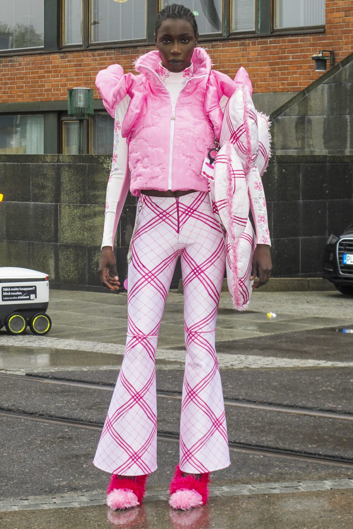 Model wearing checkered bell-bottom racing trousers, floral racing top, pink padded vest with flowers and big padded flower bag