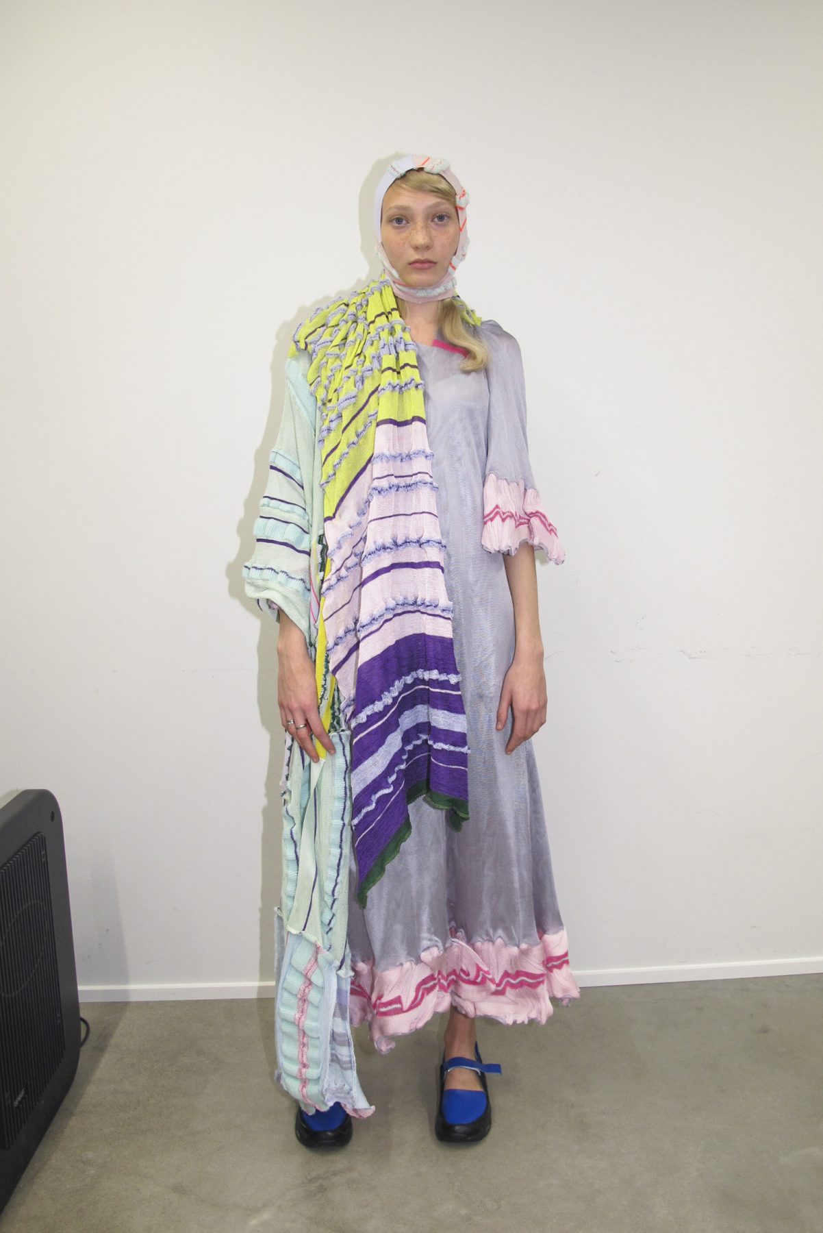 Photo of model wearing long knitted dress, patchwork scarf and blue shoes