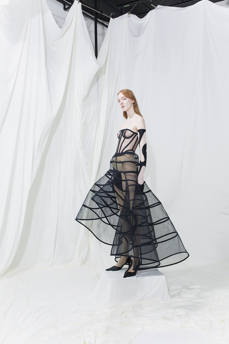 Model is wearing a black mesh fitted dress with see-through crinoline skirt. Black cut-out gloves and leggings.