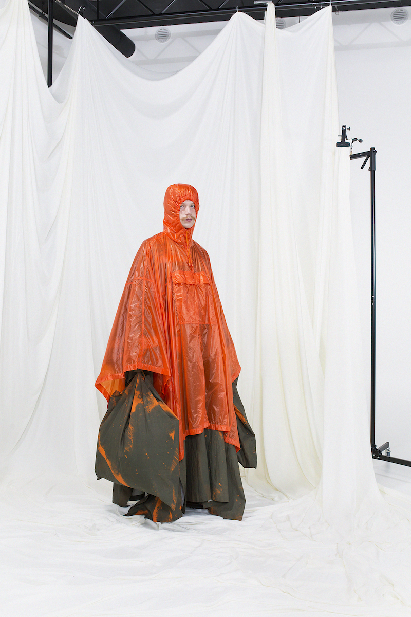 Model wearing a hooded orange nylon raincoat with green printed undercoat and bag