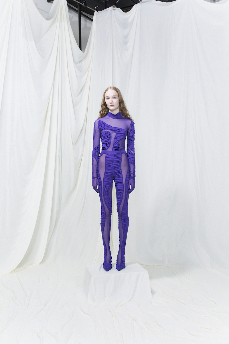 Model wearing a purple bodysuit with purple mesh cutouts.