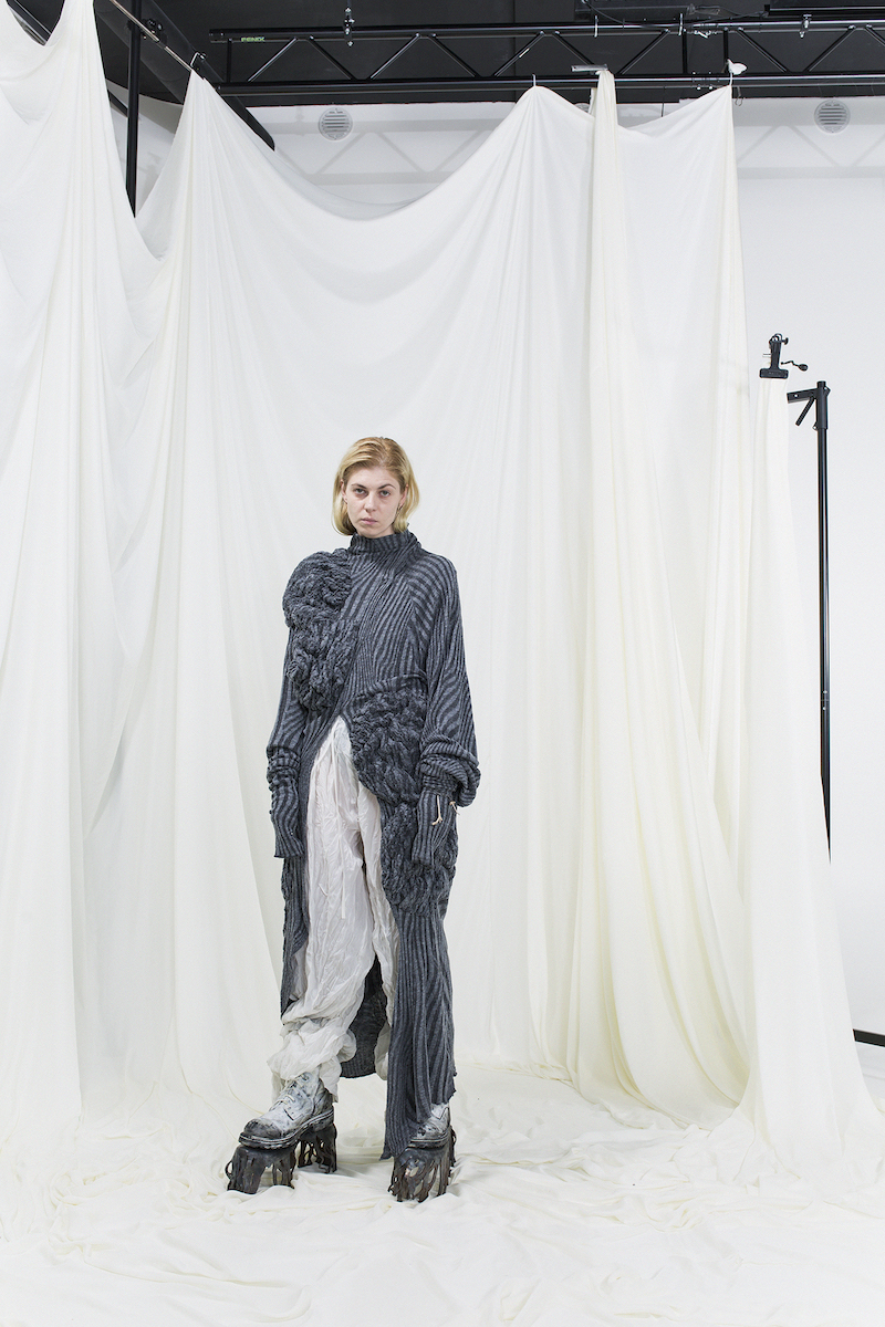 Model wearing silver and grey knitted long shirt and white crumpled trousers