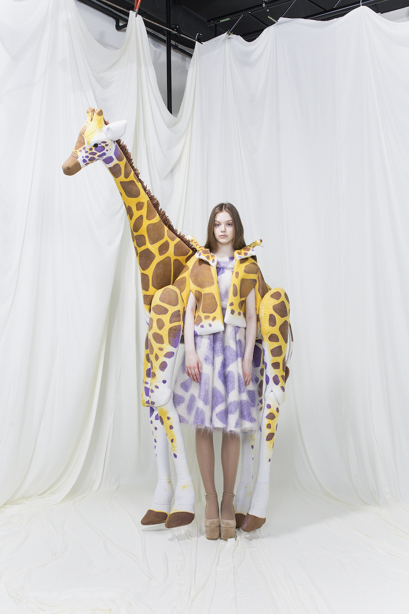 Model wearing a giraffe shaped cape with giraffe shaped collars. Giraffe printed brushed mohair dress underneath.