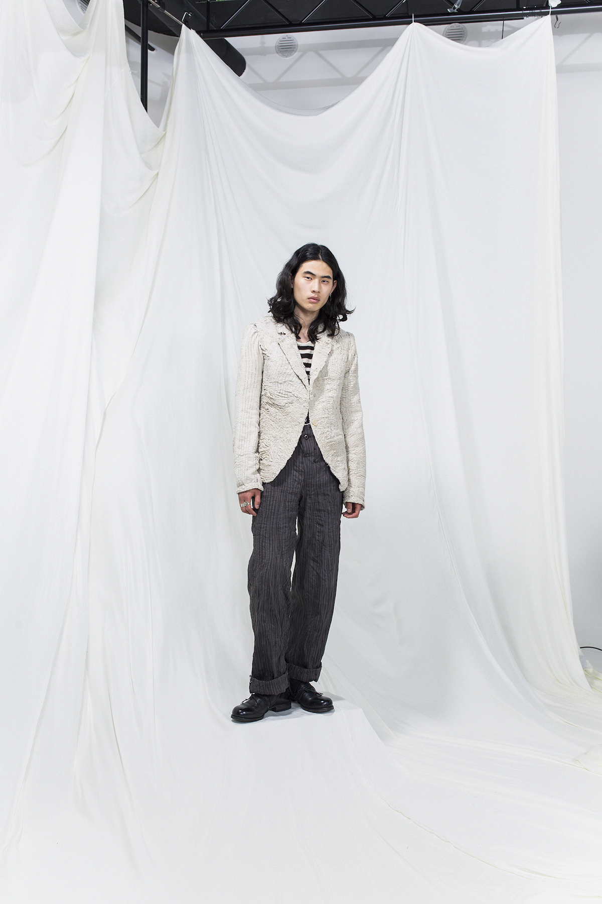 Model is wearing a striped shirt, grey oversized trousers and white crumpled blazer
