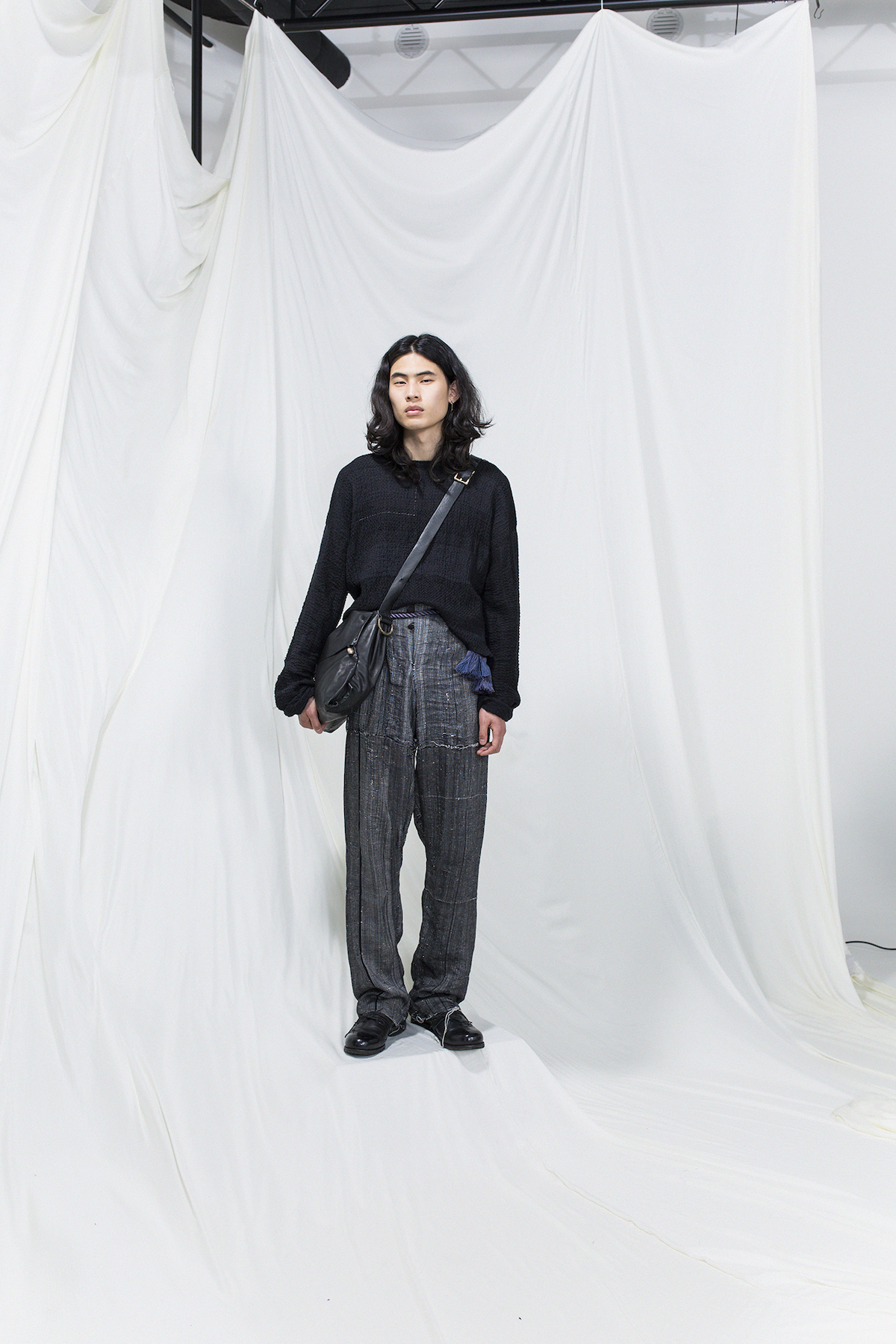 Model is wearing a oversized black sweater, oversized grey trousers and black leather crossbody bag