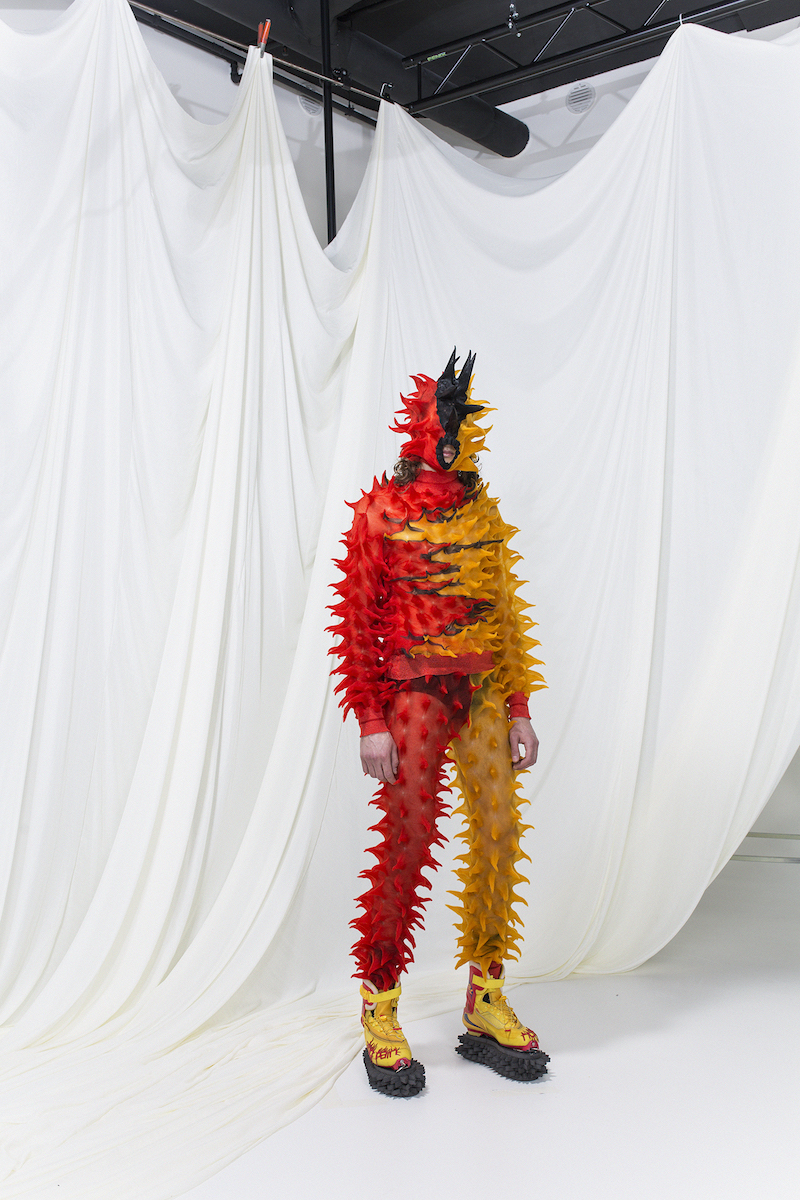 Model is wearing a half-red half- yellow spike knit sweater and sweatpants, matching mask.