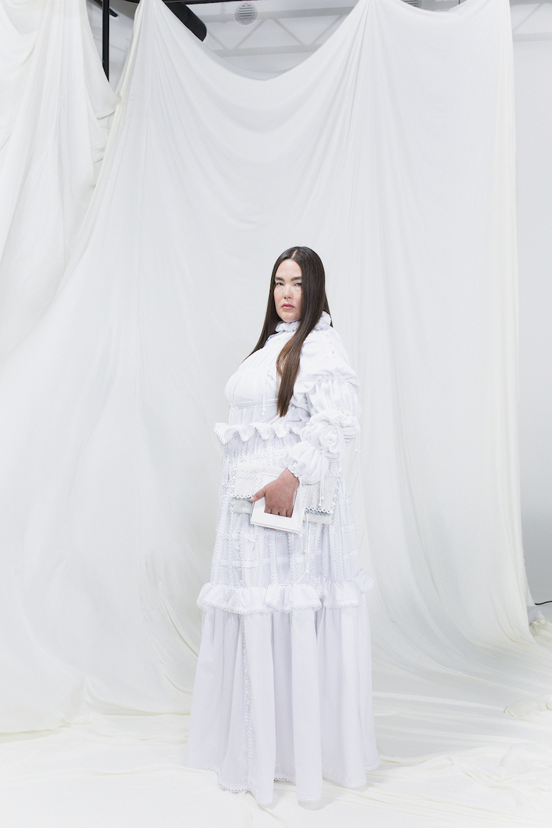Model is wearing a white modular gown with puffy sleeves and matching white clutch