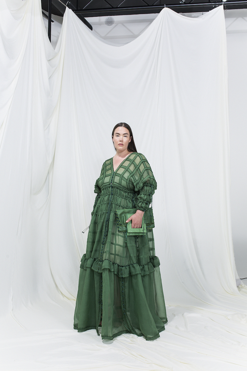 Model is wearing a green modular silk organza gown with matching green leather clutch