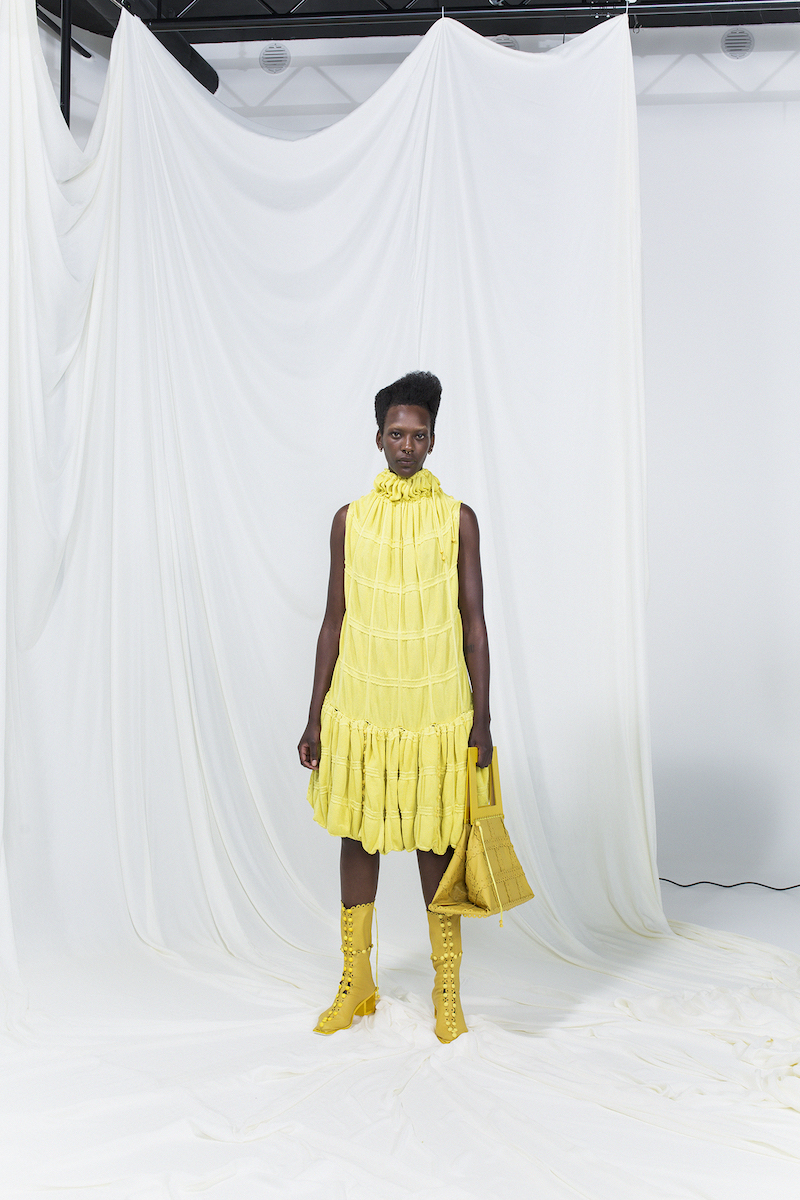 Model is wearing a yellow sleeveless modular mid-dress with matching yellow leather bag and heeled boots