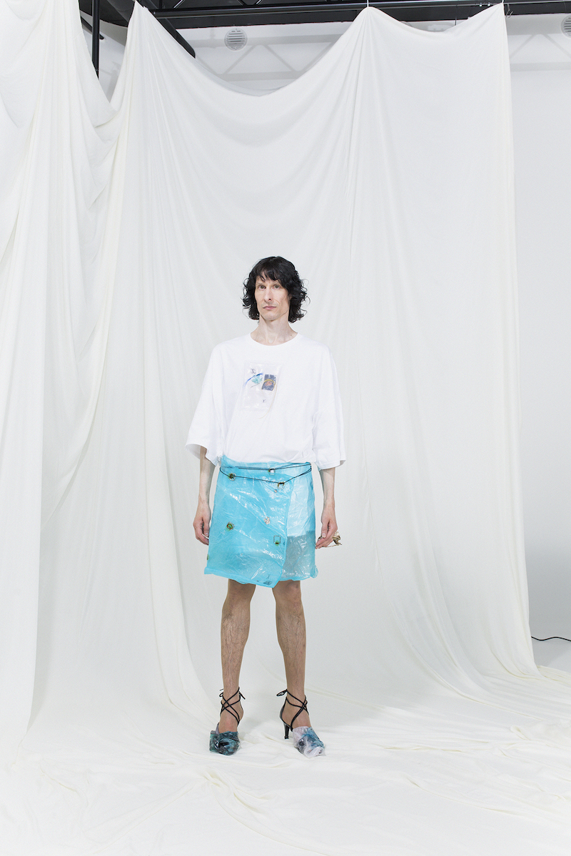 Model is wearing a white coated t-shirt and light blue wrap skirt with experimental heels