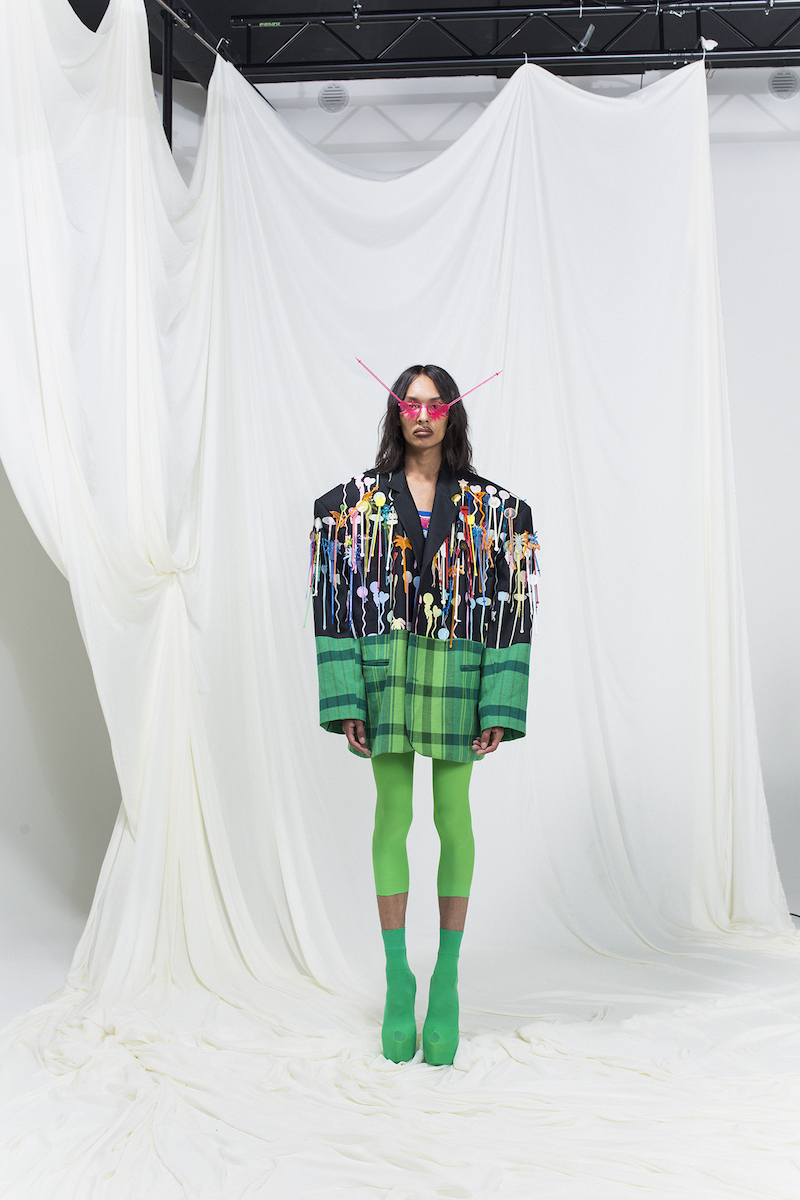 Model wearing an oversized blazer embroidered with cocktail sticks, green leggings and high heels, cocktail sticks as sunglasses.