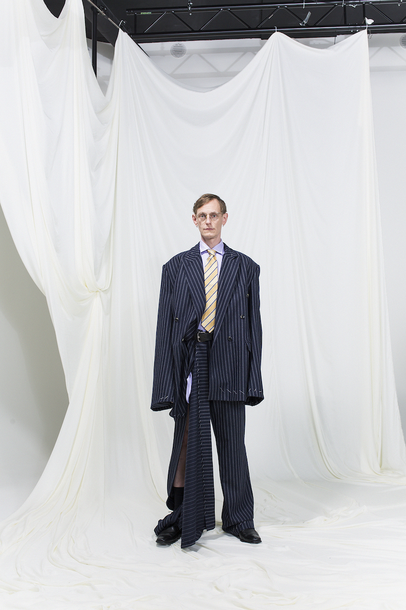 Model is wearing a pinstripe oversized suit with slit on right leg