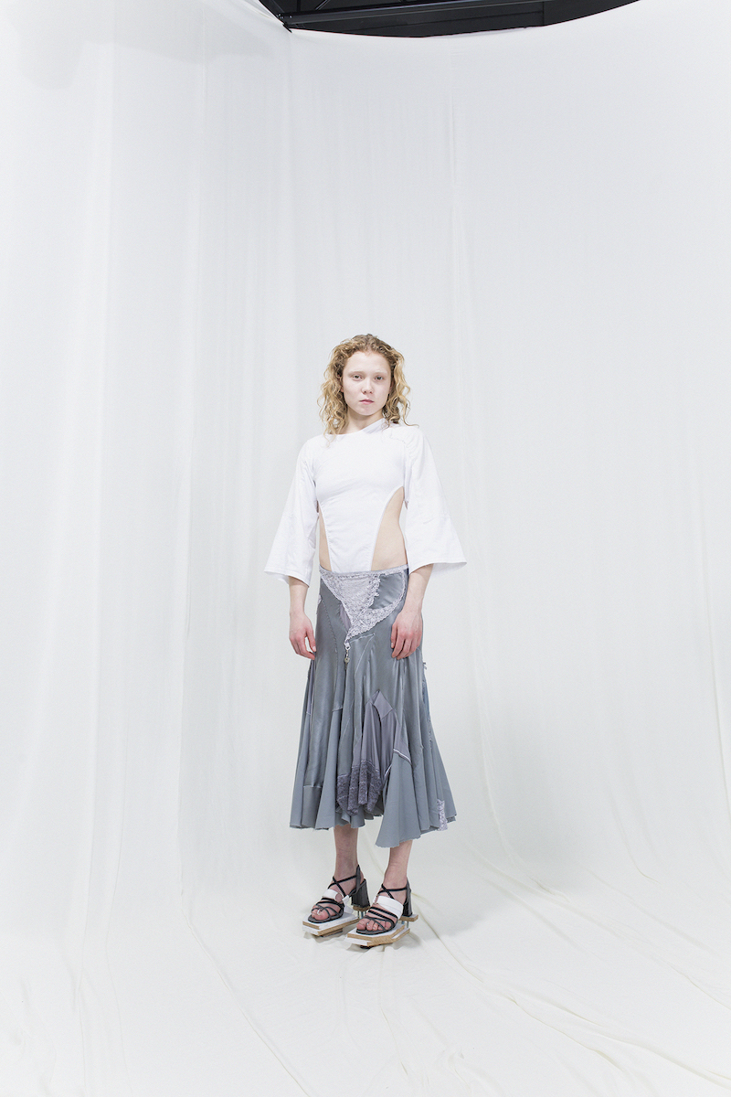Model is wearing a white 3/4 sleeved top with cuts in the front and bias-cut silver skirt