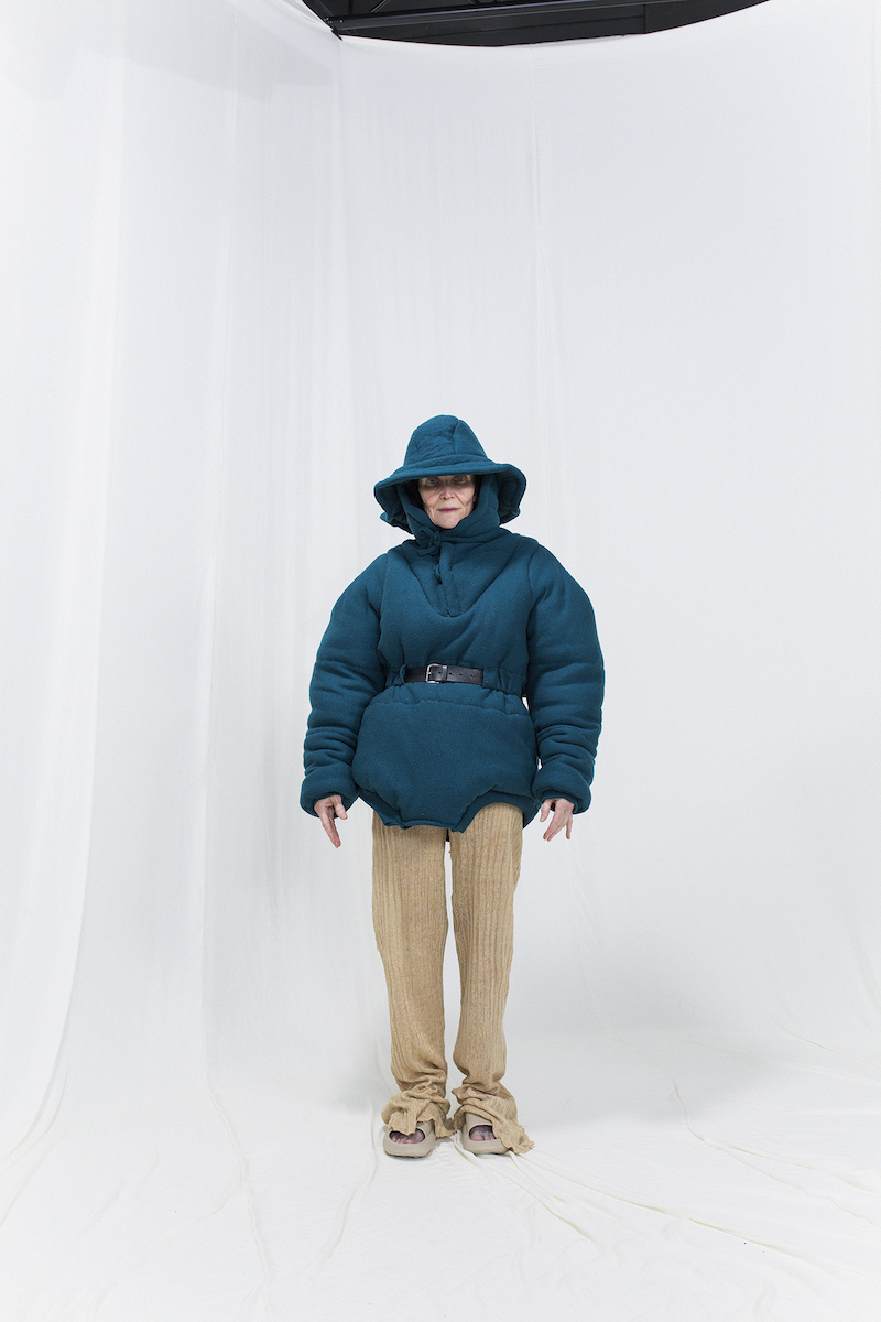 Model is wearing a petroleum blue felted anorak with hat-hood and knitted linen trousers
