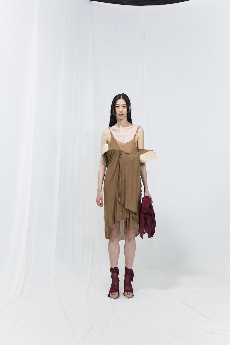 Model is wearing a brown slip-on dress with bended birch piece attached, burgundy bag