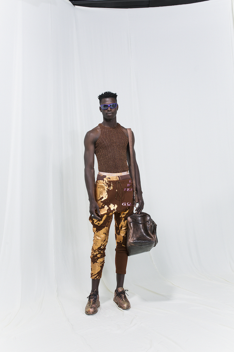 Model is wearing a brown ribbed top with brown-golden cropped trousers and oversized travel bag