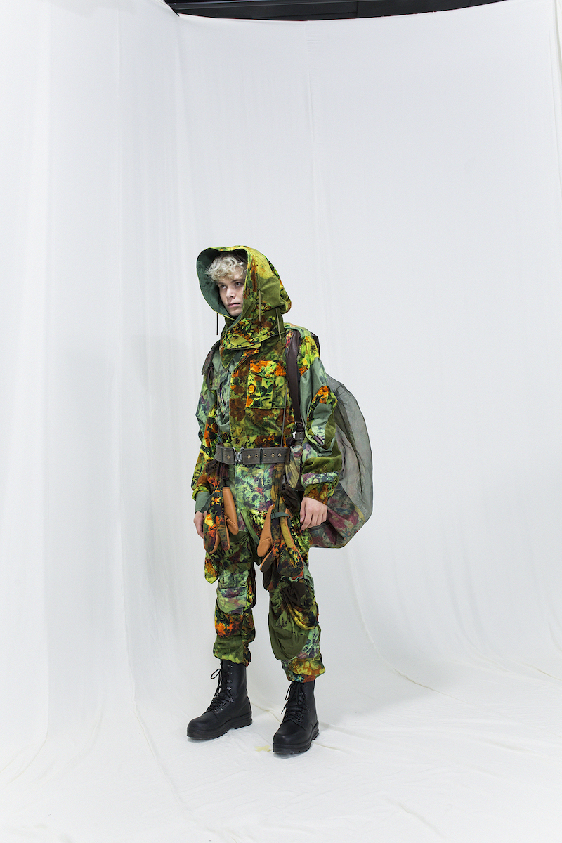 Model is wearing a multicoloured floral jacket with matching pants and a hood, see through rucksack