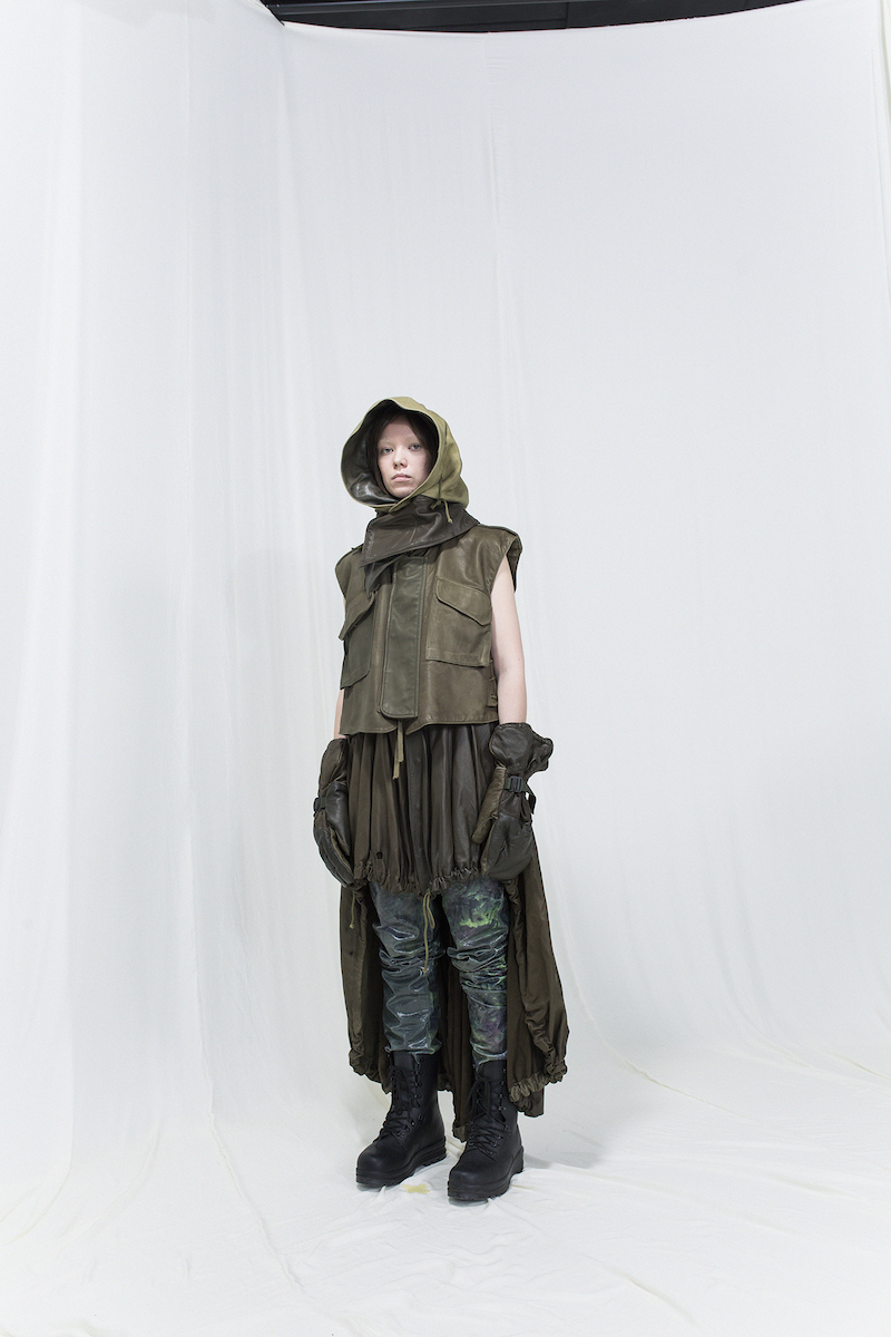 Model is wearing a multicoloured leather vest with matching hood, gloves and skirt, with glossy trousers underneath