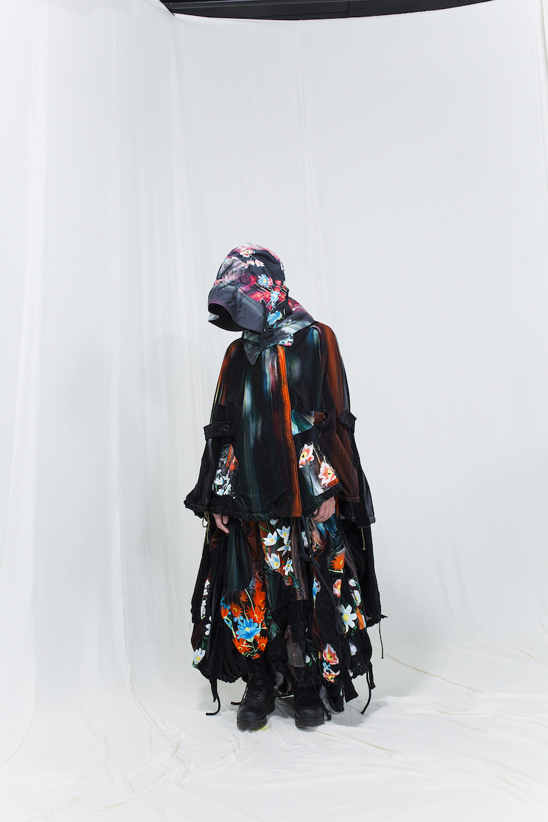 Model is wearing a multicoloured melting floral cape and skirt in velvet, matching hood