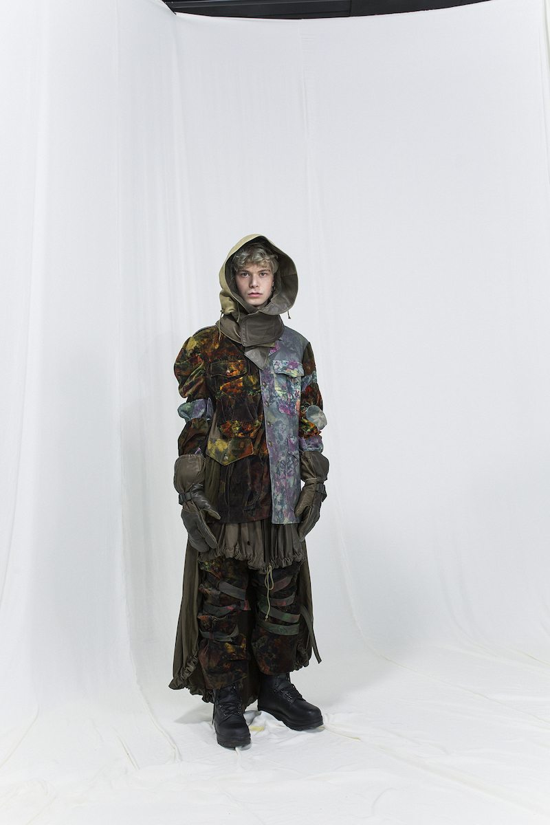 Model is wearing a multicoloured floral jacket with panels, leather hood and bondage velvet trousers underneath