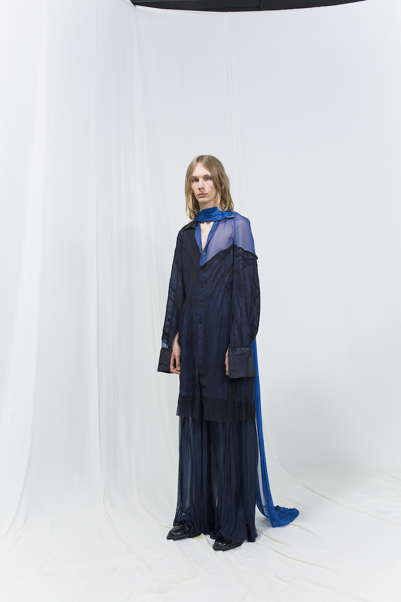 Model is wearing a long coat with sheer blue details and matching navy-blue flowy trousers