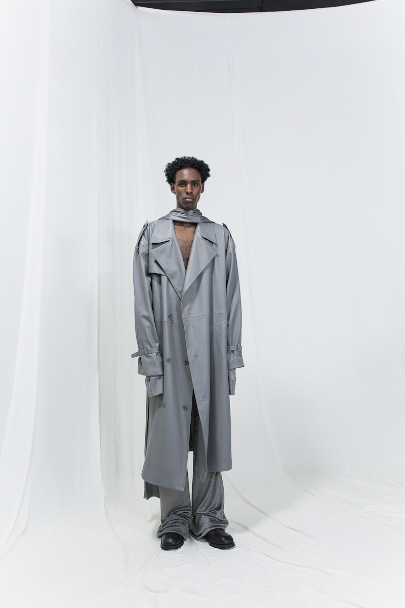 Model is wearing a long silver grey trench coat with matching trousers