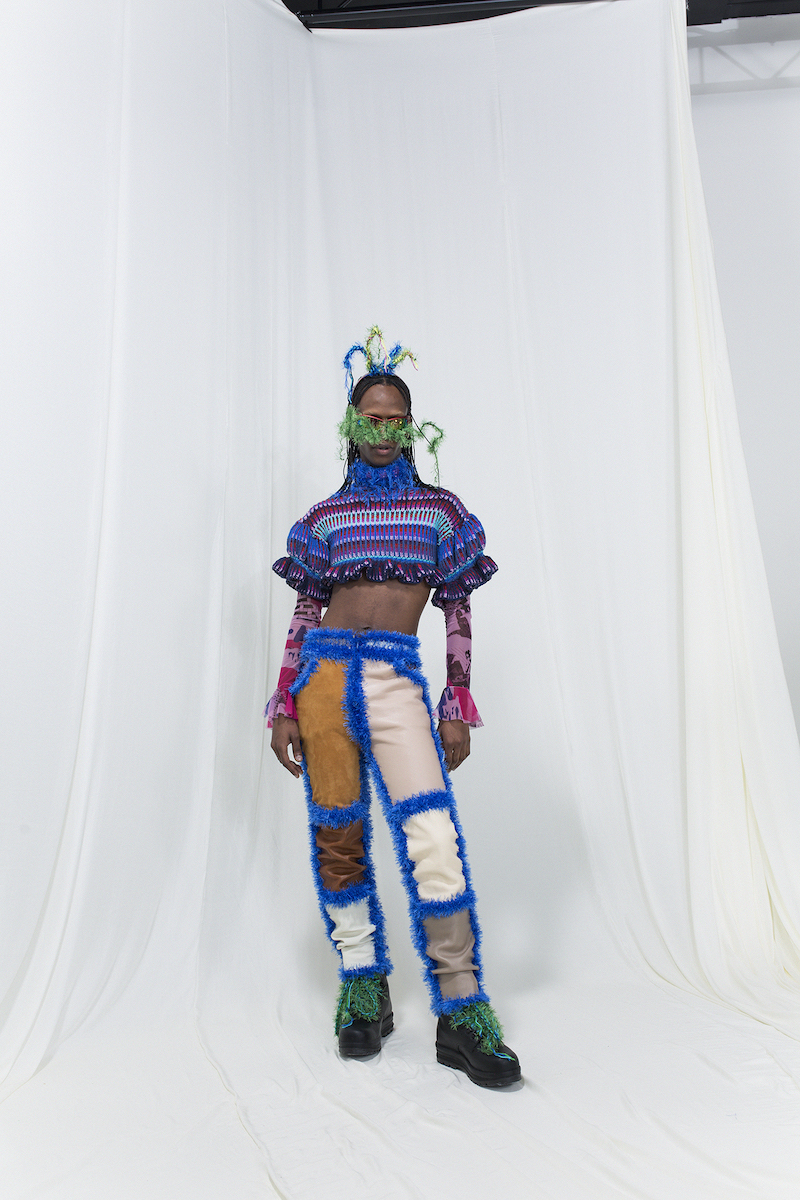 Model wearing a knitted stripe crop-top with crochet leather trousers, mesh top underneath, sunglasses and a fringed headpiece
