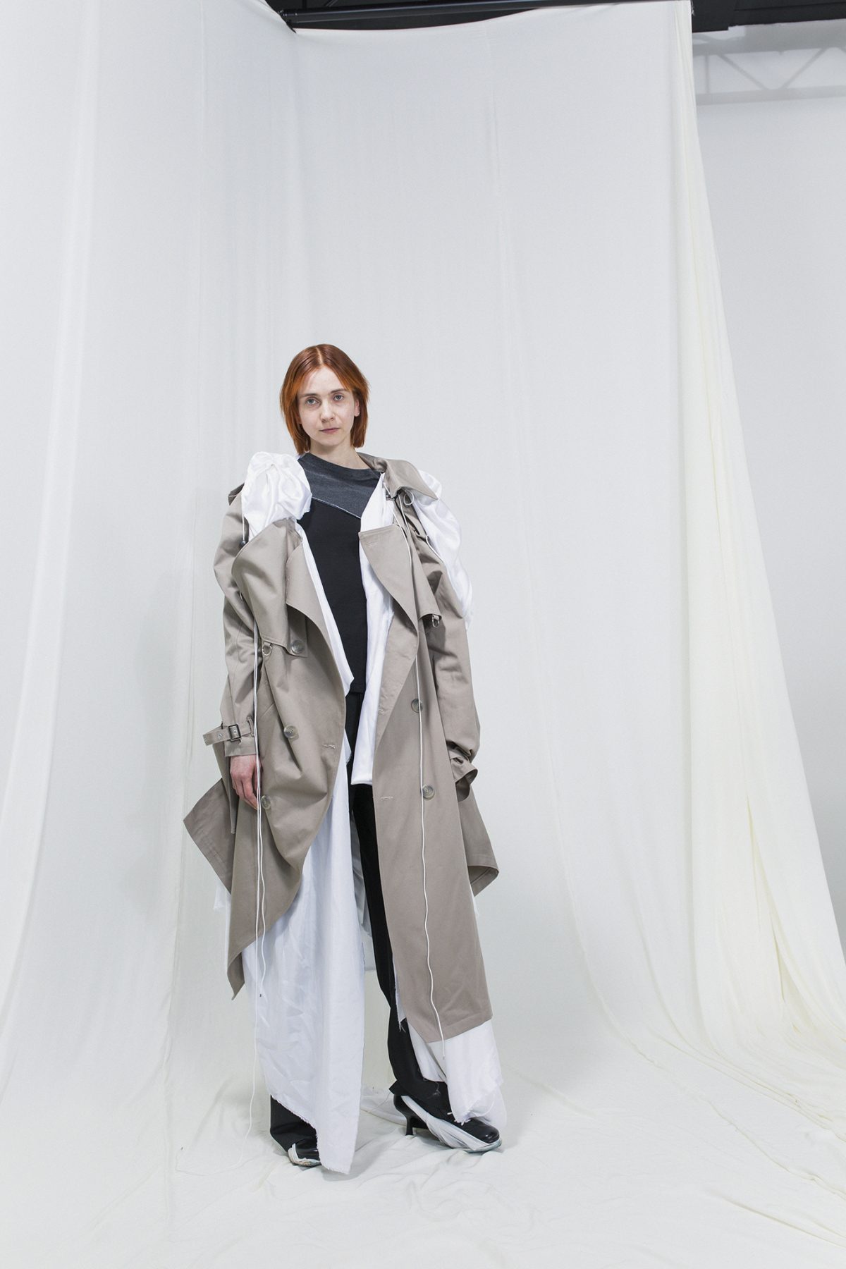 Model wearing a beige trench coat on top of a white robe, black trousers